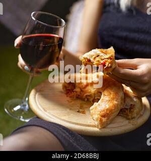 Ein Glas Leitungswein und ein Kuchen mit Gemüse in den Händen einer Frau auf einem Tablett. Gemütliche authentische Atmosphäre Stockfoto