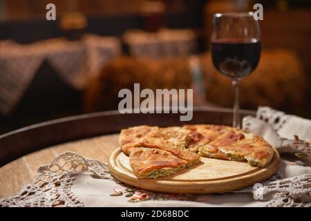 Glas Rotwein und Stücke von placida mit Quark oder Vertuta auf einem Holztablett, Nahaufnahme, traditionelle rumänische, moldawische oder Balkan-Kuchen Stockfoto