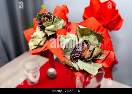 Eine verwelkte rote Rose mit einem großen roten Band, das auf einem Tisch in einer Vase steht. Stockfoto