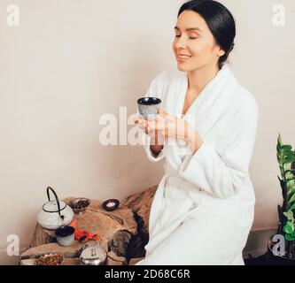 Porträt einer kaukasischen Frau in Robe, mit Teetasse, lächelnd in Spa Resort ruhend. Stockfoto