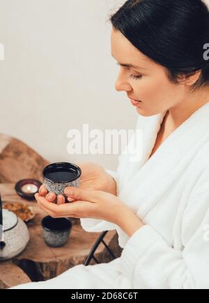 Eine gesunde 35-jährige Frau entspannt und trinkt Tee in einem Bademantel während Wellness-Wochenende Stockfoto