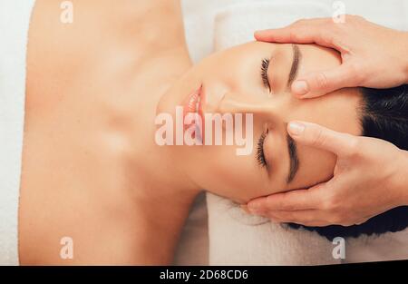 Anti-Stress-Kopfmassage. Schöne Frau bekommt eine entspannende Kopfmassage und genießt es, im Spa zu entspannen. Nahaufnahme des Gesichts, Draufsicht. Stockfoto