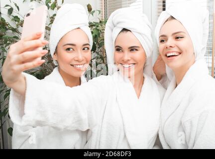 Frauen haben ein schönes Wochenende im Spa Resort. Drei schöne Frauen tragen Bademäntel und Handtücher auf dem Kopf machen Selfie, genießen Ruhe Stockfoto