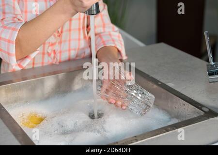 Nahaufnahme einer Frau, die ein Glas hält und ein Spülbecken mit Wasser aus einem Wasserhahn füllt. Reinigungs- und Hygienekonzept. Stockfoto