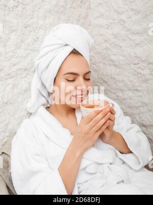 Halotherapie in einem Kurort. Schöne Frau mit Handtuch auf dem Kopf trinkt Tee im Salzraum. Salzluftbehandlung. Spa-Wochenende Stockfoto