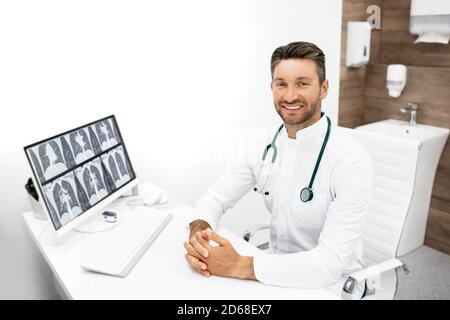 Porträt eines Arztes an seinem Arbeitsplatz in einer modernen Klinik. Therapeut mit Stethoskop in einem Arztpraxis sitzen. Ein Röntgenbild der Lunge befindet sich auf seinem Computer Stockfoto