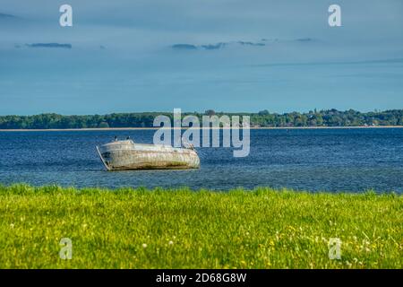 Ein hölzernes Schiffswrack, das auf seiner Seite in flachem und schlammigem Wasser liegt, vermittelt Isolation und Abgeschiedenheit. An Land gewaschene Holzboote tragen Einsamkeit und Einsamkeit Stockfoto