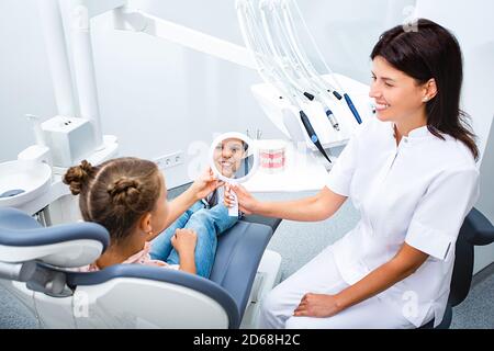 Kleines Mädchen suchen im Spiegel auf gesunde Zähne nach der Behandlung, während in einem Zahnarztstuhl sitzen. Kinderzahnarzt kommunizieren mit kleinen Patienten Stockfoto