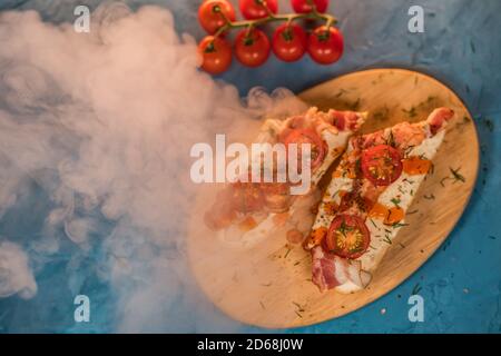 Stillleben von appetitlichen Bruschetts auf Holzbrett mit Dampf. Nahaufnahme von Sandwiches mit geschmolzenem Käse, Speck, Kirschtomaten, Dill und Sauce auf Stockfoto