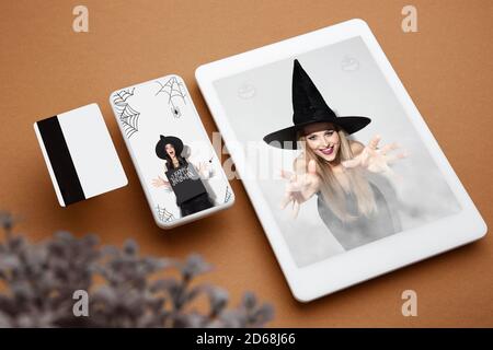 Junge Frau in schwarzem Hut auf Gerät Bildschirm und braunen Hintergrund. Attraktive kaukasische weibliche Modell. Halloween, schwarzer freitag, Cyber montag, Verkauf, Party, Herbstkonzept. Tablet und Geldkarte. Stockfoto