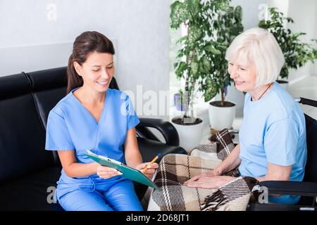 Die Krankenschwester zeigt die Testergebnisse einem älteren Patienten, der im Rollstuhl sitzt, die Tests sind normal. Rehabilitation von Menschen nach Verletzungen und Krankheiten Stockfoto