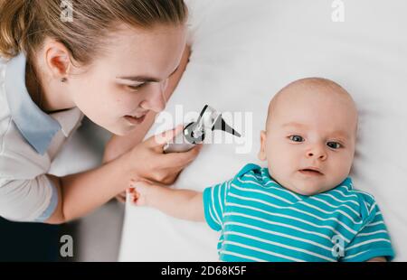 Lächelnder Kinderarzt, der eine Ohruntersuchung mit einem Otoskop bei einem Baby im Krankenhaus macht. Arzt untersucht Kleinkind im Alter von 3 Monaten Stockfoto