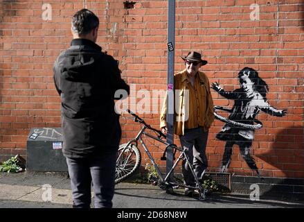 Die Bewohner von Nottingham fotografieren neben dem Graffiti-Kunstwerk, das jetzt als Werk des Straßenkünstlers Banksy bestätigt wurde, auf einer Seite eines Grundstücks an der Rothesay Avenue und der Ilkeston Road in Nottingham. Das Kunstwerk zeigt ein junges Mädchen, das mit einem Reifen spielt, und ist auf einer Wand in der Nähe eines verlassenen Fahrrads gemalt, dem ein Rad fehlt. Stockfoto