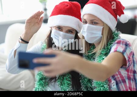 Zwei Frauen in Schutzmaske und weihnachtsmann Hut sprechen online am Telefon. Stockfoto