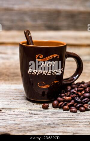 Geröstete Kaffeebohnen in der Nähe einer Tasse Kaffee isoliert auf Holztisch und Hintergrund. Stockfoto