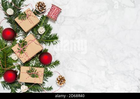 Weihnachtliche Flachlage mit handgefertigten geschenkschachteln, roten Kugeln, Nadelbaumzweigen und Tannenzapfen auf Marmorhintergrund. Geschenkverpackung. Frohe Weihnachten Stockfoto