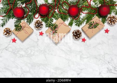 Weihnachtliche Flachlage mit handgefertigten geschenkschachteln, roten Kugeln, Nadelbaumzweigen, Tannenzapfen, Girlande, Holzsternen auf Marmorboden Stockfoto