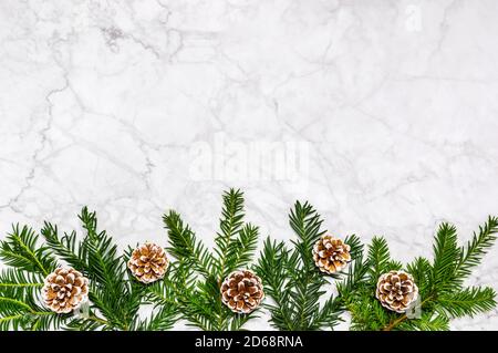 Einfache Winterflachlage mit Nadelbaumzweigen und Tannenzapfen unten auf Marmorboden. Grußkarte, Banner, Platz für Text Stockfoto