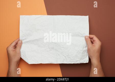 Zwei männliche Hände halten ein leeres zerknittertes Blatt weißes Papier, brauner Hintergrund Stockfoto
