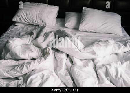 Unbemachtes, leeres Bett mit weißer Bettwäsche. Bettwäsche und Kissen im Apartment oder Hotel nach einer Nacht schlafen. Dreckige und zerknitterte Decke im Hotel Stockfoto