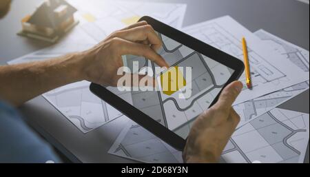 Mann, der Baugrundstück sucht, um auf Katasterplan für zu kaufen Hausbau auf digitalem Tablet Stockfoto