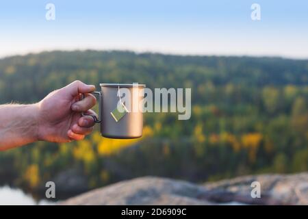 Ein Mann hält eine Tasse Tee in der Hand vor dem Hintergrund eines Herbstwaldes. Stockfoto