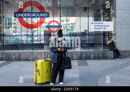 London, Großbritannien. 15. Oktober 2020. Eine Frau mit Gesichtsmast steht neben ihrem Koffer vor der Victoria U-Bahnstation. Derzeit ist die England Warnstufe: Tier 1, Medium (die Regel von sechs gilt innen und außen, Pubs und Restaurants geschlossen um 22 Uhr), Aber um zu versuchen, die Coronavirus-Pandemie weiter zu kontrollieren, hat die britische Regierung heute angekündigt, dass ab Samstag die Hauptstadt, sowie andere Regionen in Großbritannien, wird auf die strengere England Warnstufe bewegen :Tier 2, High Credit: Stephen Chung/Alamy Live News Stockfoto