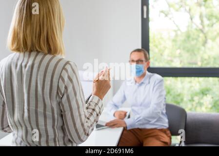 Die Frau gibt eine Präsentation und der Mann trägt die Gesichtsmaske. Zwei Kollegen in der Firma tragen eine Gesichtsmaske bei einem Meeting während der Coronav-Konferenz Stockfoto