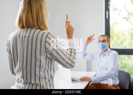 Die Frau gibt eine Präsentation und der Mann trägt die Gesichtsmaske. Zwei Kollegen in der Firma tragen eine Gesichtsmaske bei einem Meeting während der Coronav-Konferenz Stockfoto