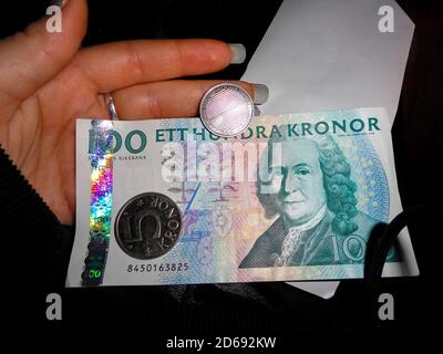 Schwedische Währung Hunderte von Banknoten und Münzen in der Hand. Dunkler Hintergrund. Stockfoto