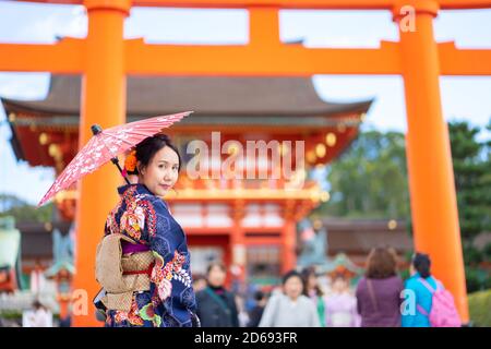 Geishas Mädchen mit japanischen kimono unter roten Holz- Tori Gate bei Fushimi Inari Schrein in Kyoto, Kimono ist ein traditionelles japanisches Gewand. Das Wort " Stockfoto
