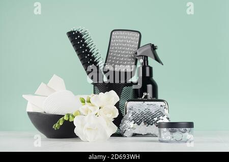 Schwarze Accessoires und Kosmetik zum Baden und Duschen weiße frische weiße Blumen Freesia in eleganten grünen Minze menthe Interieur auf weißem Holztisch. Stockfoto