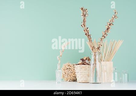 Einfaches Bio beige Holz Wohndekor mit getrockneten Pflanzen in Glasflaschen, Zweige Haufen, Weidenkorb in grüner Minze menthe Farbe Interieur auf weißem Tab Stockfoto