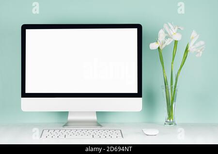 Spring Home Office für Unternehmen mit leerem pc, Tastatur, Maus und weißen frischen Blumen in Glasvase in hellgrünen Mint menthe Interieur auf weißem Holz Stockfoto