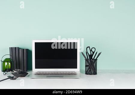 Spring Office Interior - Arbeitsplatz mit leerem Laptop-Display, schwarzer Schreibwaren, Bücher, Glas Kerzenständer in hellgrün mint menthe Interior auf weiß Stockfoto