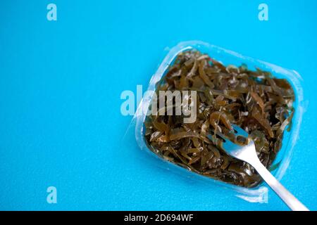 Ein köstlicher frischer Algensalat. Essbarer Algensalat und Gabel auf blauem Hintergrund. Stockfoto