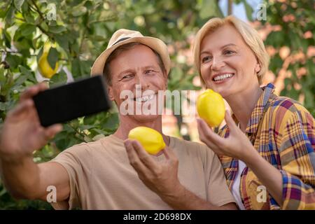 Lächelndes Paar mittleren Alters hält Zitronen, macht Selfie Stockfoto