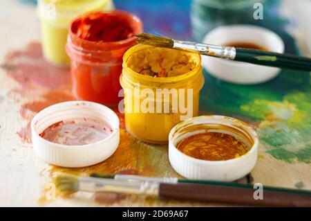 Pinsel für das Zeichnen und mehrere offene Gläser Gouache von Auf der Palette bleiben verschiedene Farben erhalten Stockfoto
