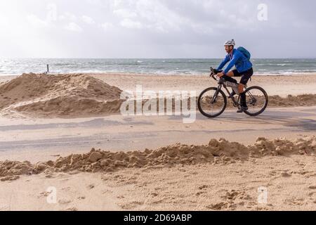 Ein eingeflügelter Radfahrer fährt entlang der Promenade zwischen Sandhaufen, die während eines Unwetters bei Southbourne in Bournemouth vom Strand geblasen worden waren. 18. Oktober 2019. Foto: Neil Turner Stockfoto