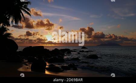 Majestätischer Sonnenuntergang am tropischen Tusculum Beach, Mahe Island, Seychellen mit Sonne bedeckt von Wolken über Horizont und sichtbaren Sonnenstrahlen. Stockfoto