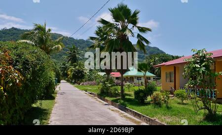 Straße mit Palmen und Ferienhäuser (touristische Unterkünfte) im Dorf auf der Insel La Digue, Seychellen. Stockfoto