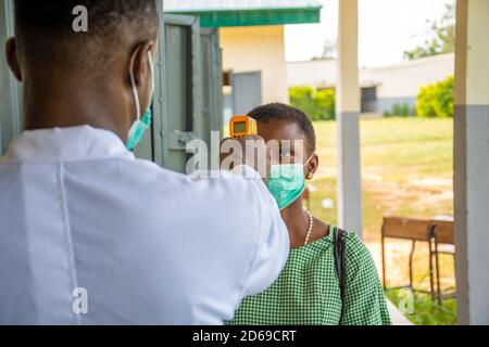 Ein Lehrer in einer afrikanischen Schule, der die Körpertemperatur des Schülers überprüft Bevor sie das Klassenzimmer betritt Stockfoto