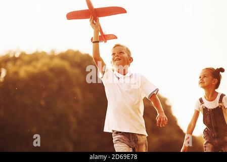 Mädchen und Junge mit Spaß im Freien mit roten Spielzeug Flugzeug In Händen Stockfoto