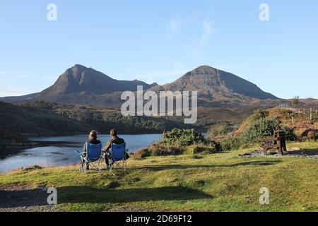 Zwei Personen genießen die Aussicht auf die Quinag Range, die über Loch A' Chàirn Bhàin, Assynt, NW Highlands of Scotland, UK, betrachtet wird Stockfoto