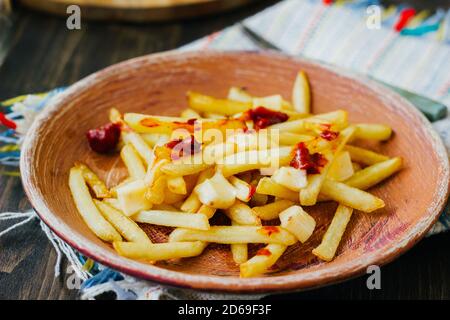 Pommes frites auf schwarzer Oberfläche anprittieren. Kanadisches Gericht mit Kartoffeln, Käse und Sauce Stockfoto