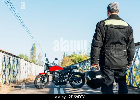 Mann auf dem Rücken, der ein Motorrad mit einem anschaut Helm in der Hand Stockfoto