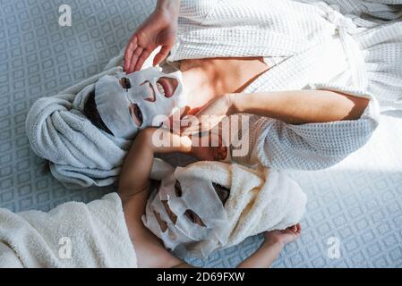 Mutter und Tochter haben Kurtag mit Schönheitsmasken auf Gesichtern. Liegen auf dem Bett mit Handtüchern auf dem Kopf Stockfoto