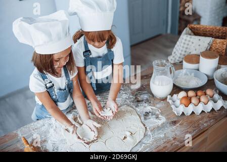 Konzentration beim Kochen. Familienkinder in weißer Chefuniform bereiten Essen in der Küche zu Stockfoto