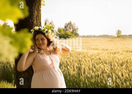 Eine schwangere Frau in einem rosa Kleid geht in der Natur. Die werdende Mutter genießt die Schwangerschaft. Stockfoto