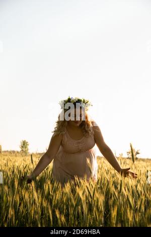 Eine schwangere Frau in einem rosa Kleid geht in der Natur. Die werdende Mutter genießt die Schwangerschaft. Stockfoto